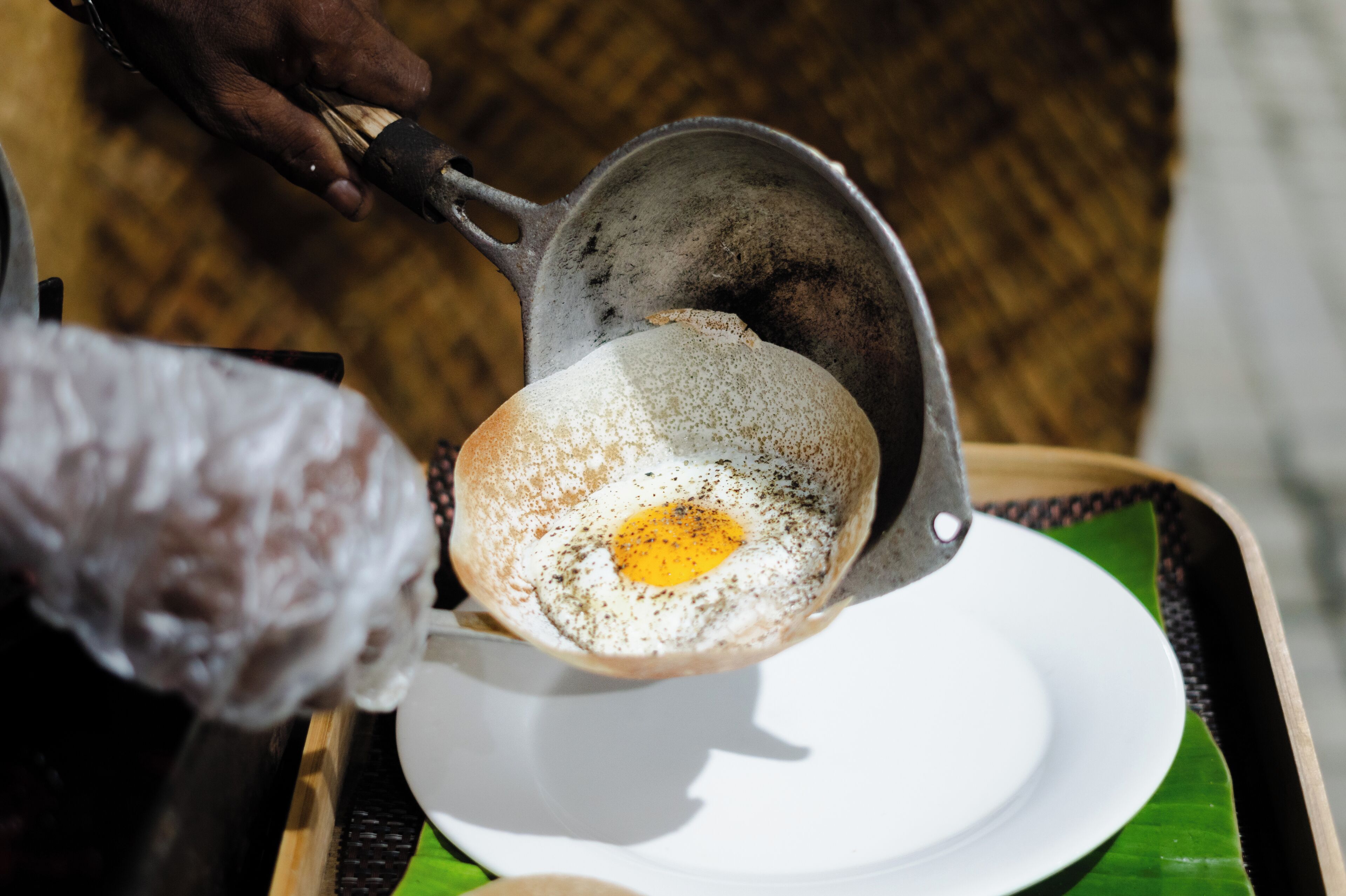 Une personne verse un œuf frit d’un bol en métal sur une assiette blanche.