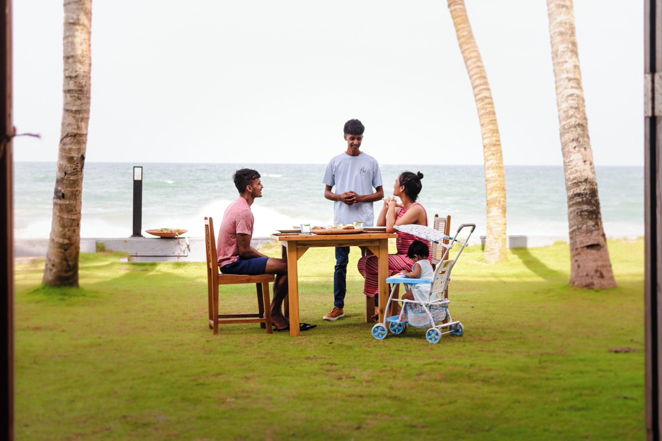 A family dining outdoors with a view of the ocean, a table, chairs, and a stroller.