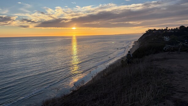 A coastal sunset view with a beach and a distant town. - Lillie’s Oceanview RUSTIC Boho Surf Cottage 
Steps to the beach & fun! (Summerland)