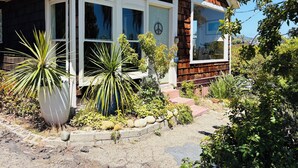 A house with a covered porch, a chimney, and a garden with various plants. - Lillie’s Oceanview RUSTIC Boho Surf Cottage 
Steps to the beach & fun! (Summerland)