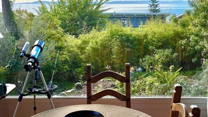 A telescope on a tripod, a wooden chair, and a view of the sea and mountains. - Lillie’s Oceanview RUSTIC Boho Surf Cottage 
Steps to the beach & fun! (Summerland)