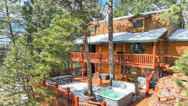A cabin with a deck, hot tub, and outdoor seating area surrounded by trees. - Log Lodge (Woodland Park)