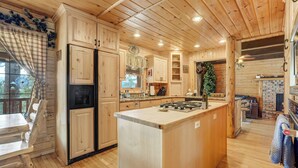 A wooden cabin interior with a kitchen featuring a central island, wooden cabinets, and a fireplace. - Log Lodge (Woodland Park)
