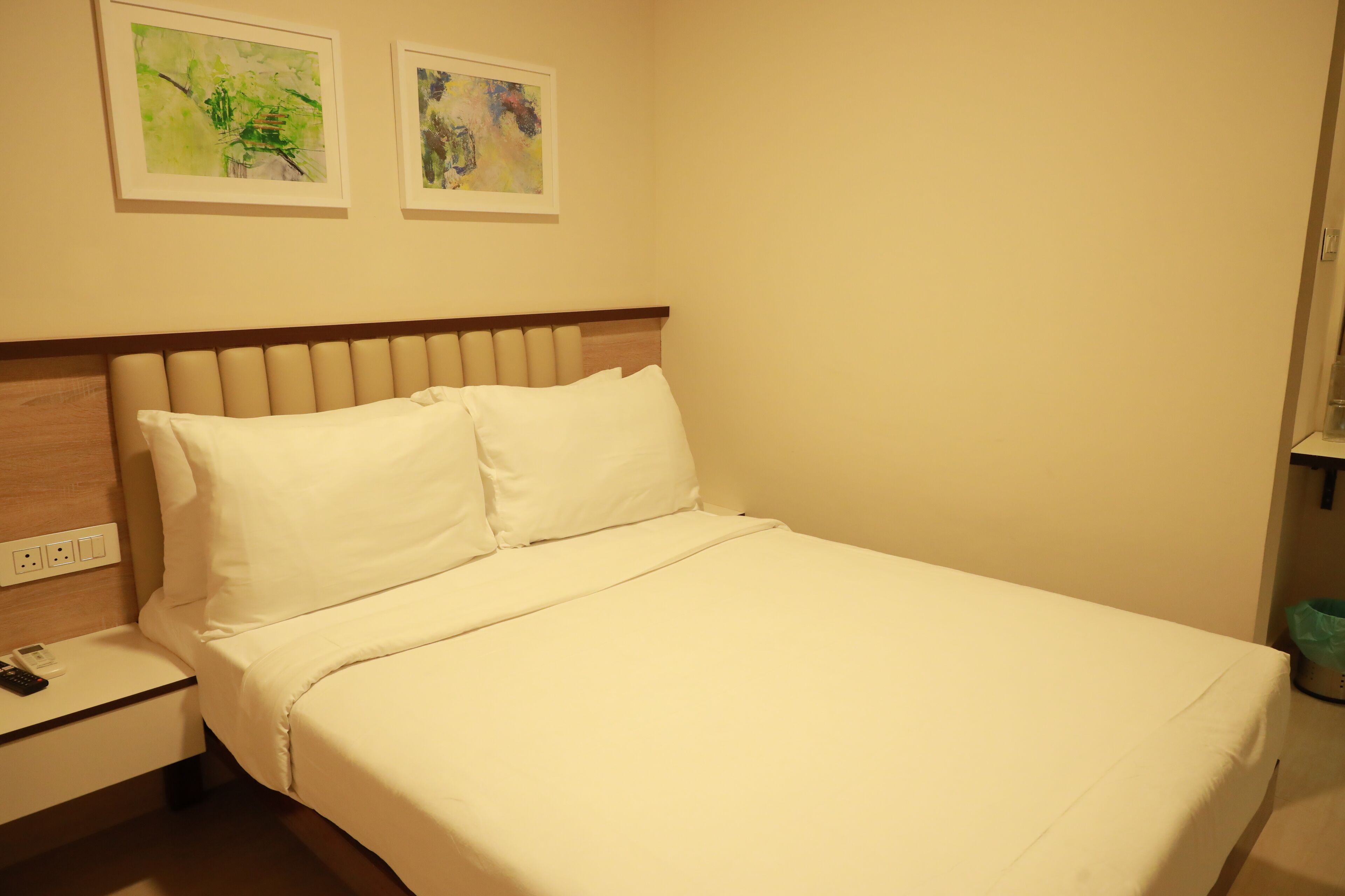 A neatly made bed with white linens, a wooden headboard, and two framed artworks on the wall.
