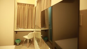 Un dormitorio pequeño con cama, espejo, una silla y una ventana con cortinas.