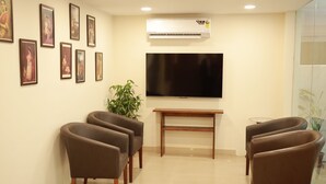 Un área de espera con televisor de pantalla plana, fotografías enmarcadas en la pared y sillones de cuero marrón.