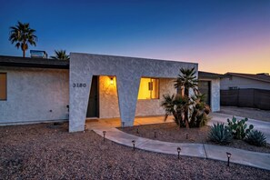 A modern house with a stucco exterior, numbered 3180, featuring a front entrance with a door and windows, surrounded by a gravel driveway and small desert plants. - Luxcation Lake Havasu Stay (Lake Havasu City)