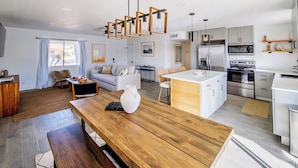 A modern kitchen with a central island, stainless steel appliances, and a dining area with a wooden table and benches.