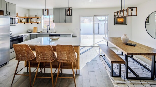 A modern kitchen with a central island, wooden chairs, and a dining table with benches.