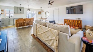 A modern living room with a sofa, a dining area with chairs, a kitchen with cabinets, and a TV mounted on the wall.