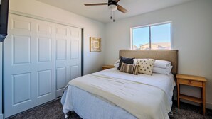 A bedroom with a bed, a window, a ceiling fan, and a door.