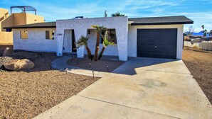 A modern single-story house with a garage, a small front yard with palm trees, and a clear blue sky.