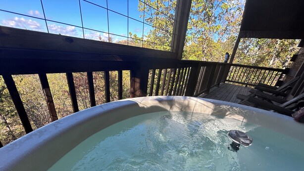 Een hottub met een houten terras en uitzicht op bomen.