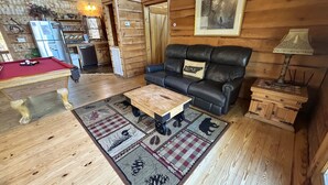 Een gezellig houten blokhutinterieur met een pooltafel, leren bank en een eethoek.