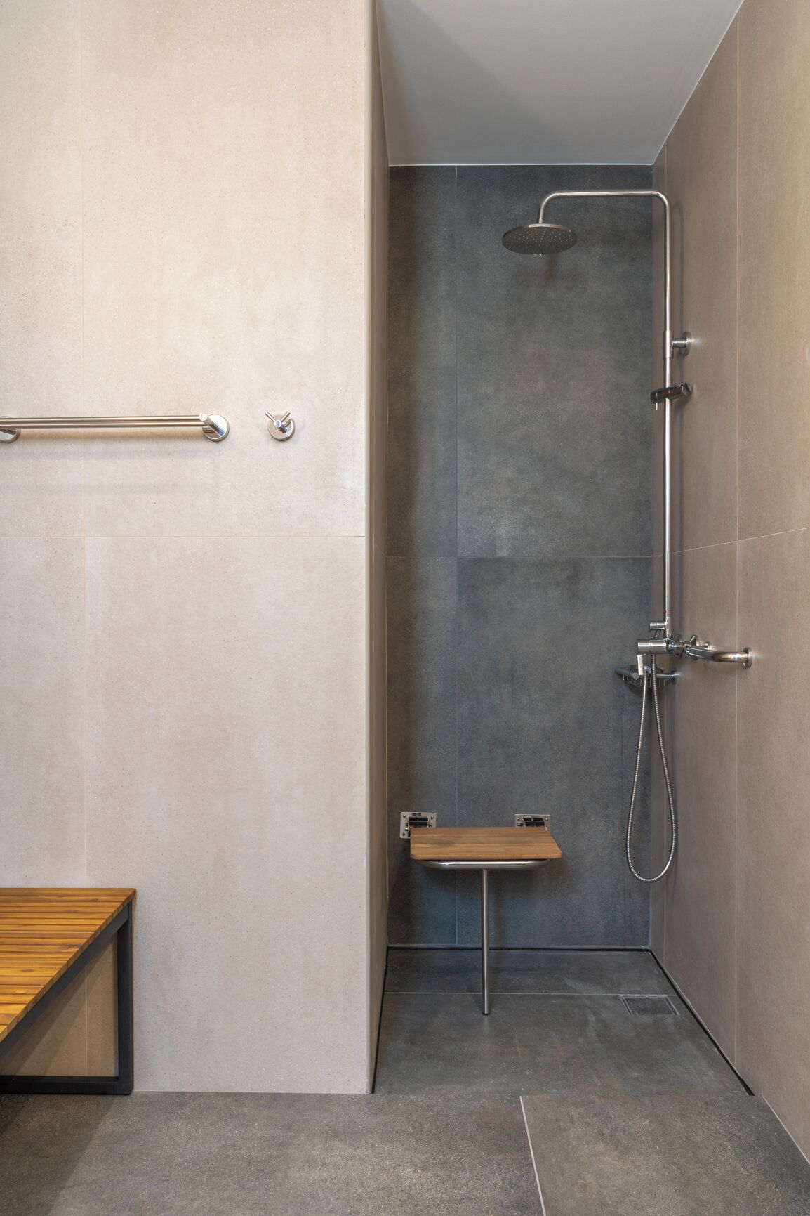 Un baño moderno con ducha, un banco de madera y una barra de apoyo.