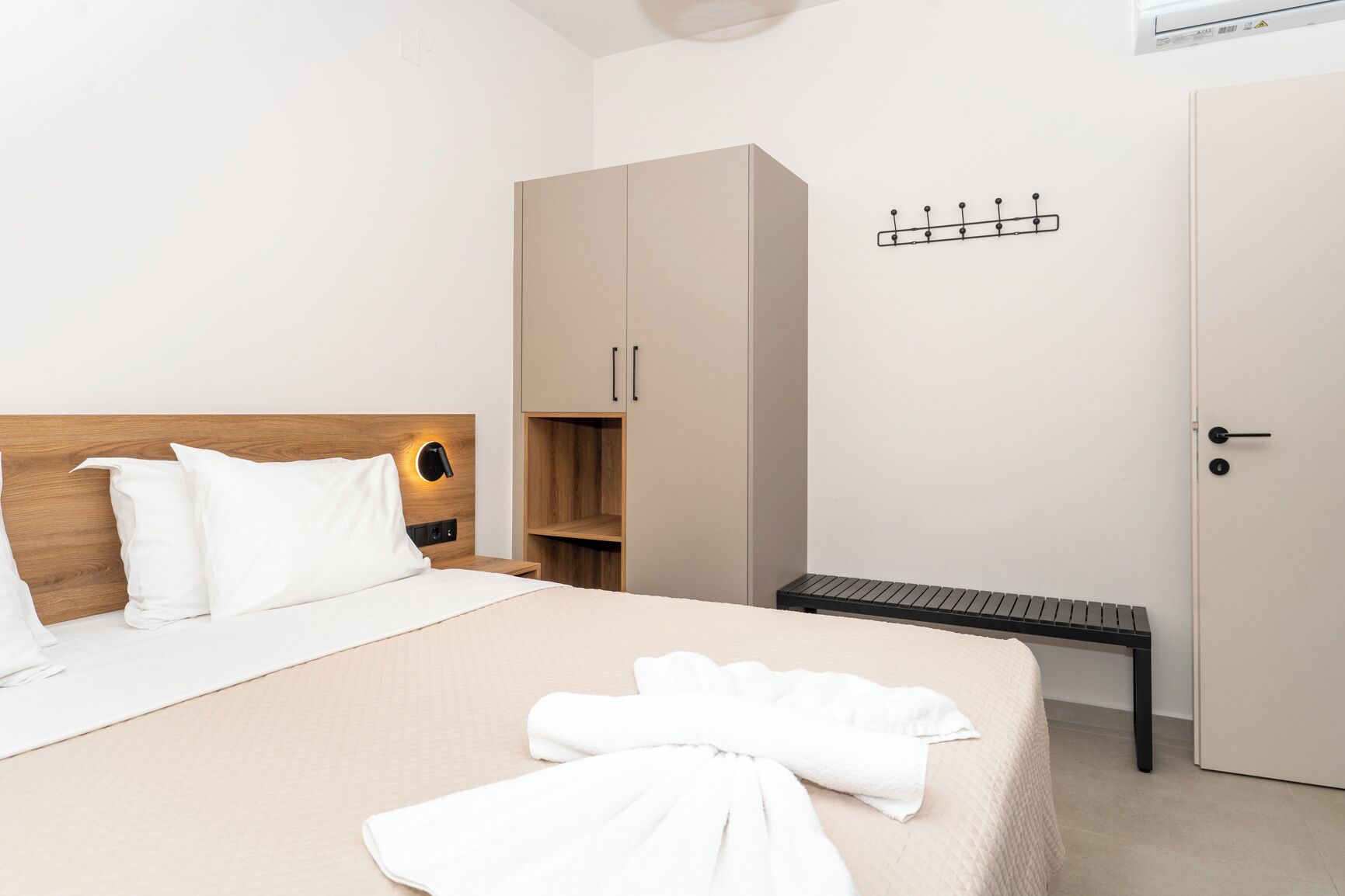 A hotel room with a bed, a wardrobe, a bench, and a coat rack.