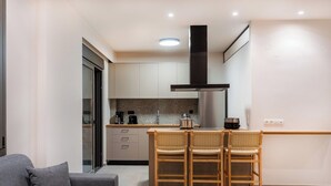 A modern kitchen with white cabinets, a stainless steel range hood, and a dining area with wicker chairs. - Dreta Suites Chania (Chania)