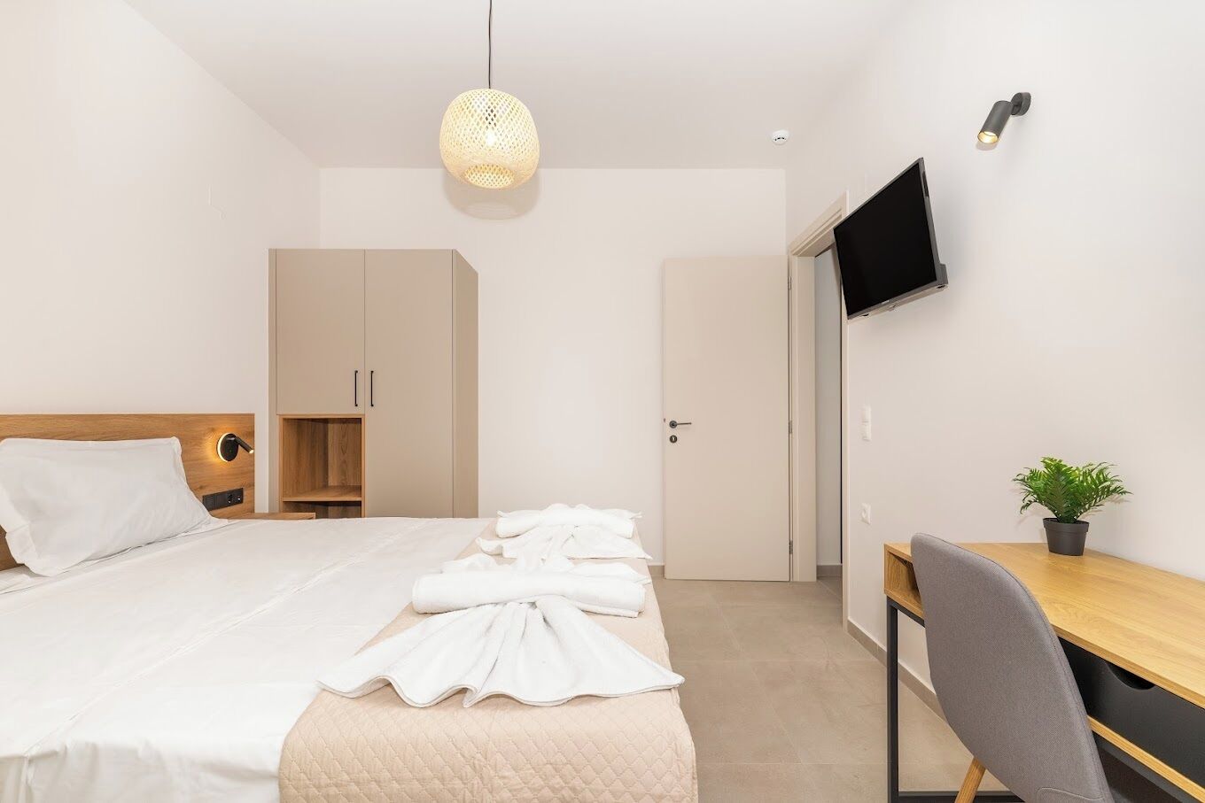 Et moderne hotelværelse med seng, skrivebord, stol, fjernsyn og en potteplante.