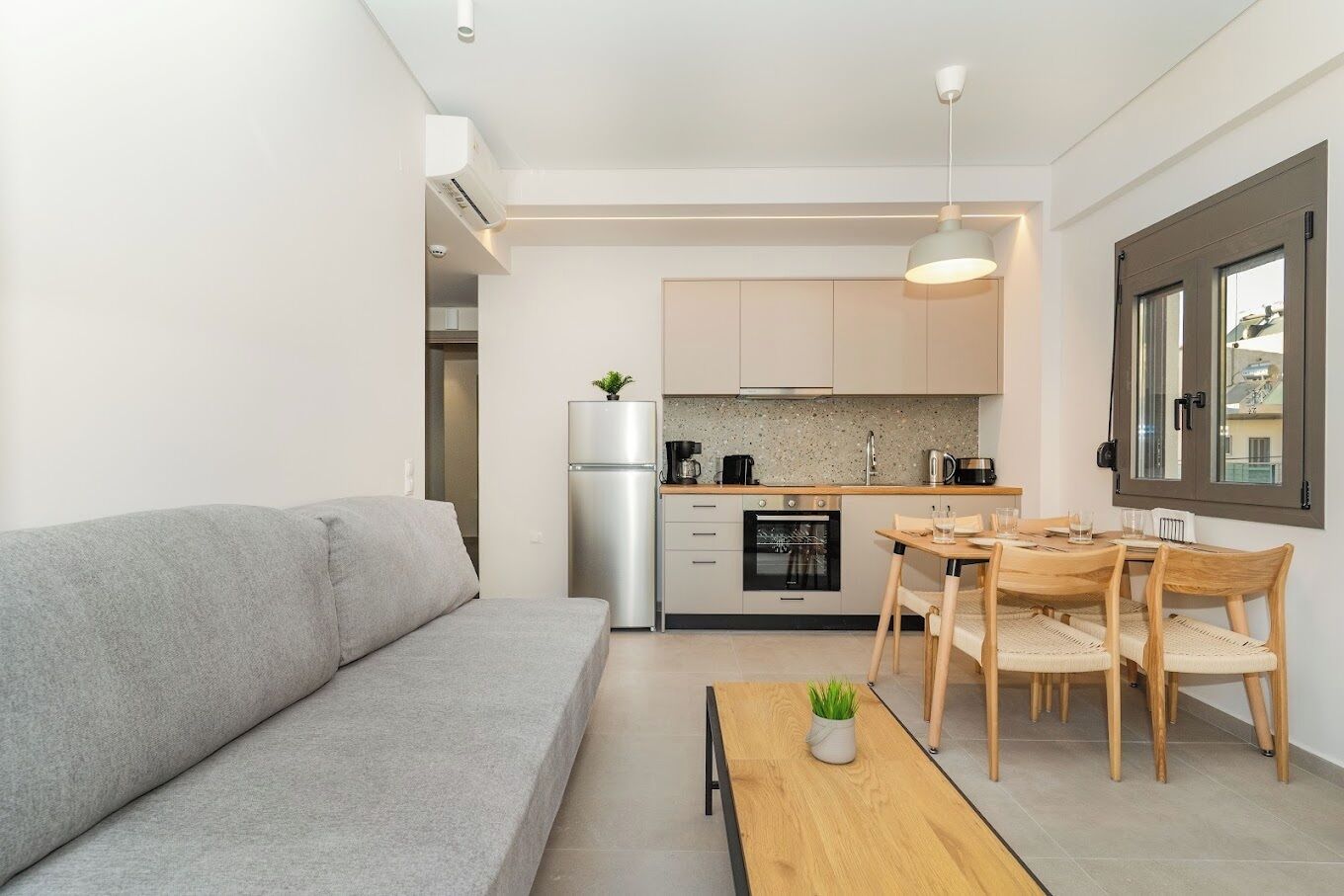 A modern kitchen with a dining area, a grey sofa, and a small table with a plant.