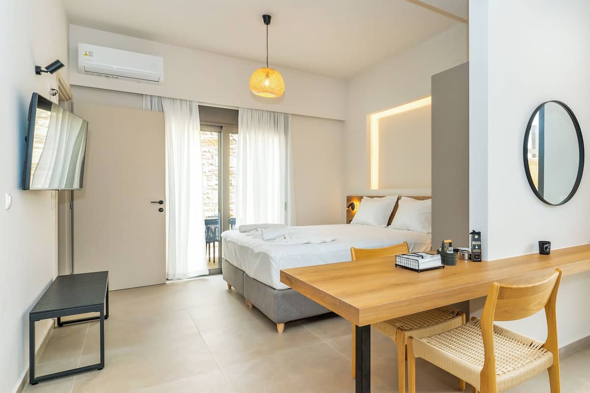 Ein modernes Hotelzimmer mit einem Bett, einem Holztisch, einem Stuhl, einem kleinen Tisch, einem Spiegel und einer Klimaanlage.