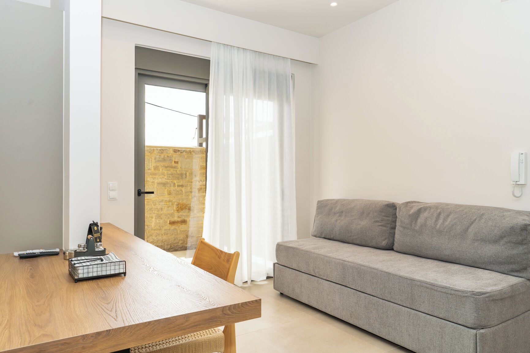 Una sala moderna con una mesa de comedor de madera, un sofá gris y vistas a una pared de piedra a través de un ventanal.