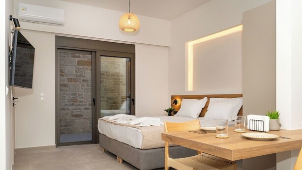 A modern bedroom with a bed, bedside table, and a TV mounted on the wall. - Dreta Suites Chania (Chania)