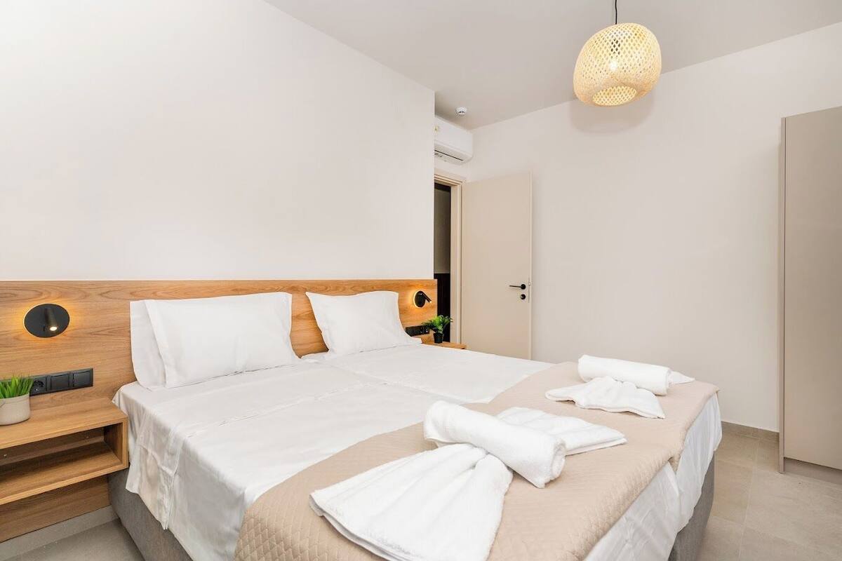 Ein modernes Hotelzimmer mit einem hölzernen Kopfteil, einem großen Bett mit weißen Bettwäsche, einem Nachttisch mit Pflanze und einer Pendelleuchte.