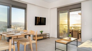 A modern, well-lit living room with a dining area, large windows, and a sliding glass door leading to a balcony. - Dreta Suites Chania (Chania)