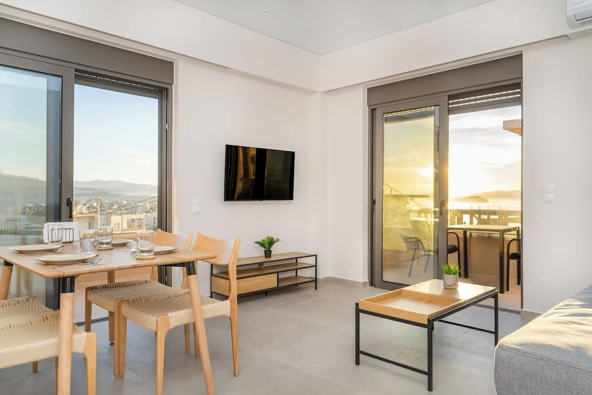 Ein modernes, helles Wohnzimmer mit Essbereich, großen Fenstern und einer Schiebetür, die auf einen Balkon führt.