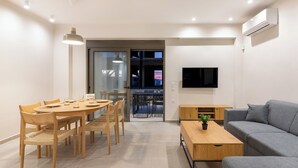 A modern living room with a grey sofa, a wooden coffee table, a dining table with chairs, and a TV mounted on the wall. - Dreta Suites Chania (Chania)
