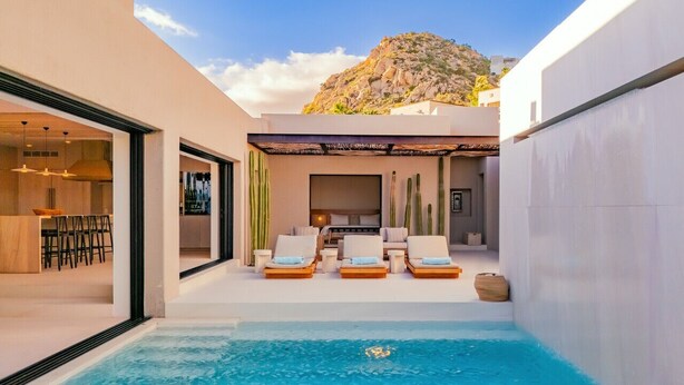 Un área de piscina moderna al aire libre con sillones de descanso, un comedor y vistas a la montaña.