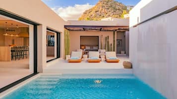 A modern outdoor pool area with lounge chairs, a dining area, and a view of a mountain.