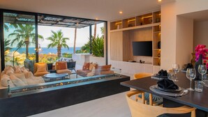 Una sala de estar moderna con un amplio ventanal que da al mar, amueblada con sofás y una mesa de comedor dispuesta para una comida.