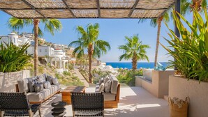 Una terraza con mesas al aire libre, vistas al mar y palmeras.