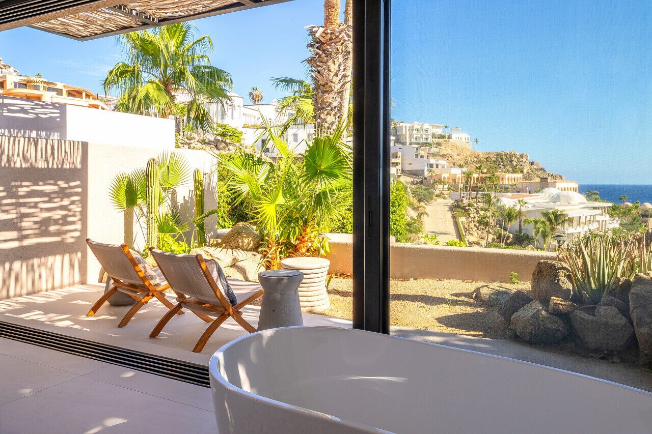 A balcony with a white bathtub, two lounge chairs, and potted plants.
