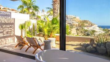 A balcony with a white bathtub, two lounge chairs, and potted plants.