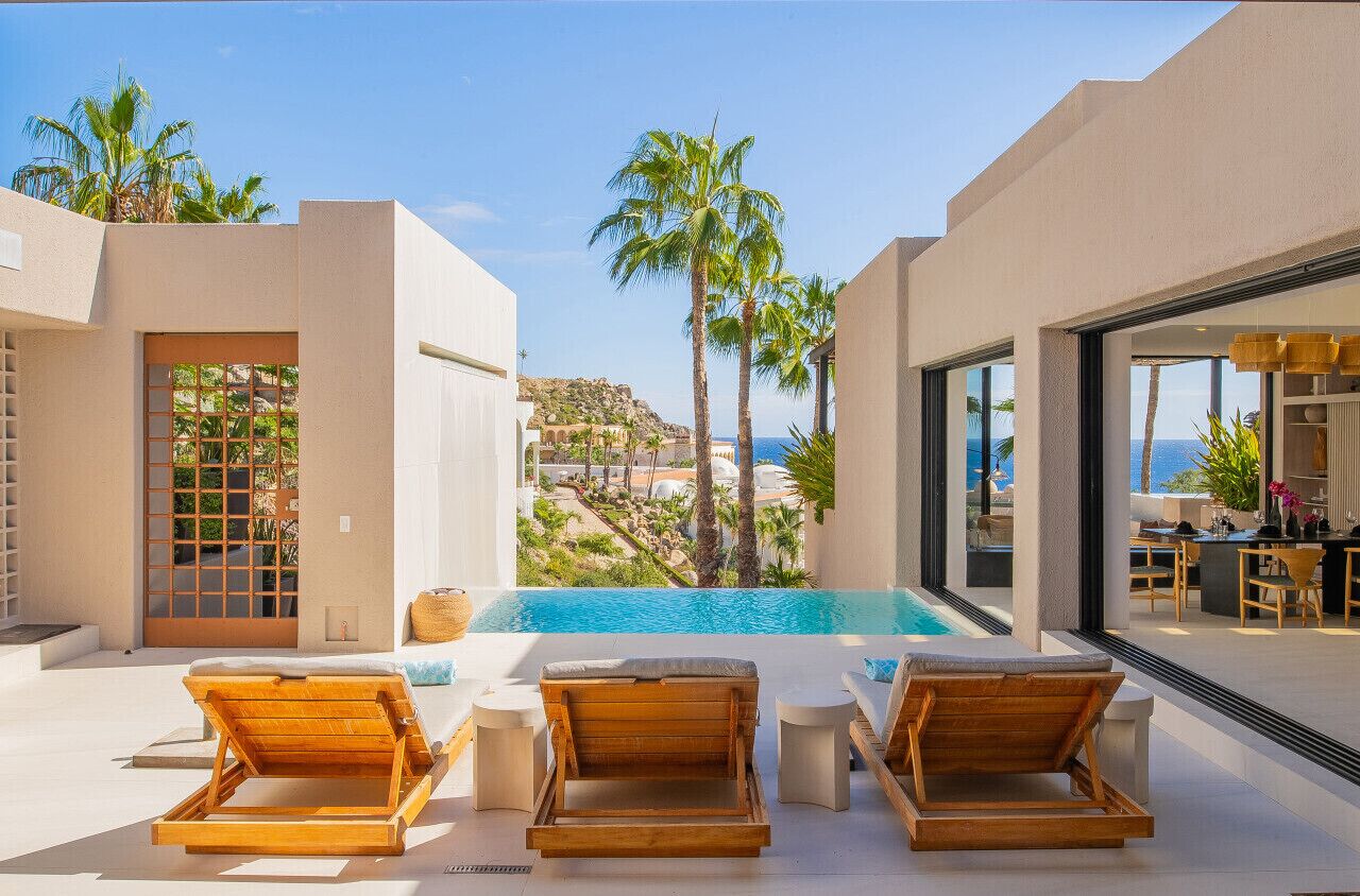A modern pool area with wooden loungers, a clear view of the sea, and a dining area with outdoor seating.