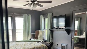 Un dormitorio con cama, ventilador de techo, televisión y un espejo grande.