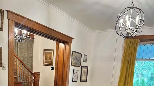 Un salón amplio con pisos de madera, un sofá grande y oscuro, una mesa de centro de vidrio y una araña.