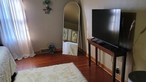 Une chambre à coucher avec un lit, un tapis moelleux, un téléviseur posé sur un meuble, un miroir et une fenêtre avec des rideaux.