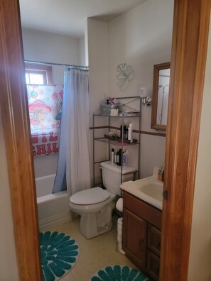 A bathroom with a toilet, a shower curtain, a shelf with toiletries, and a wooden cabinet. - Charming 3-bedroom house with AC, WiFi in pleasant Hardwick.   (Hardwick)