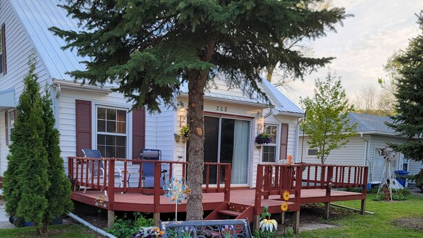 Une maison avec un porche, un banc et un arbre.