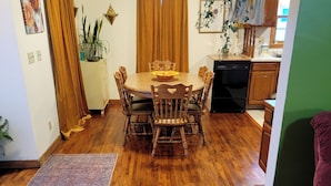 Un coin repas avec une table et des chaises en bois, une cuisine en arrière-plan et un mur vert.