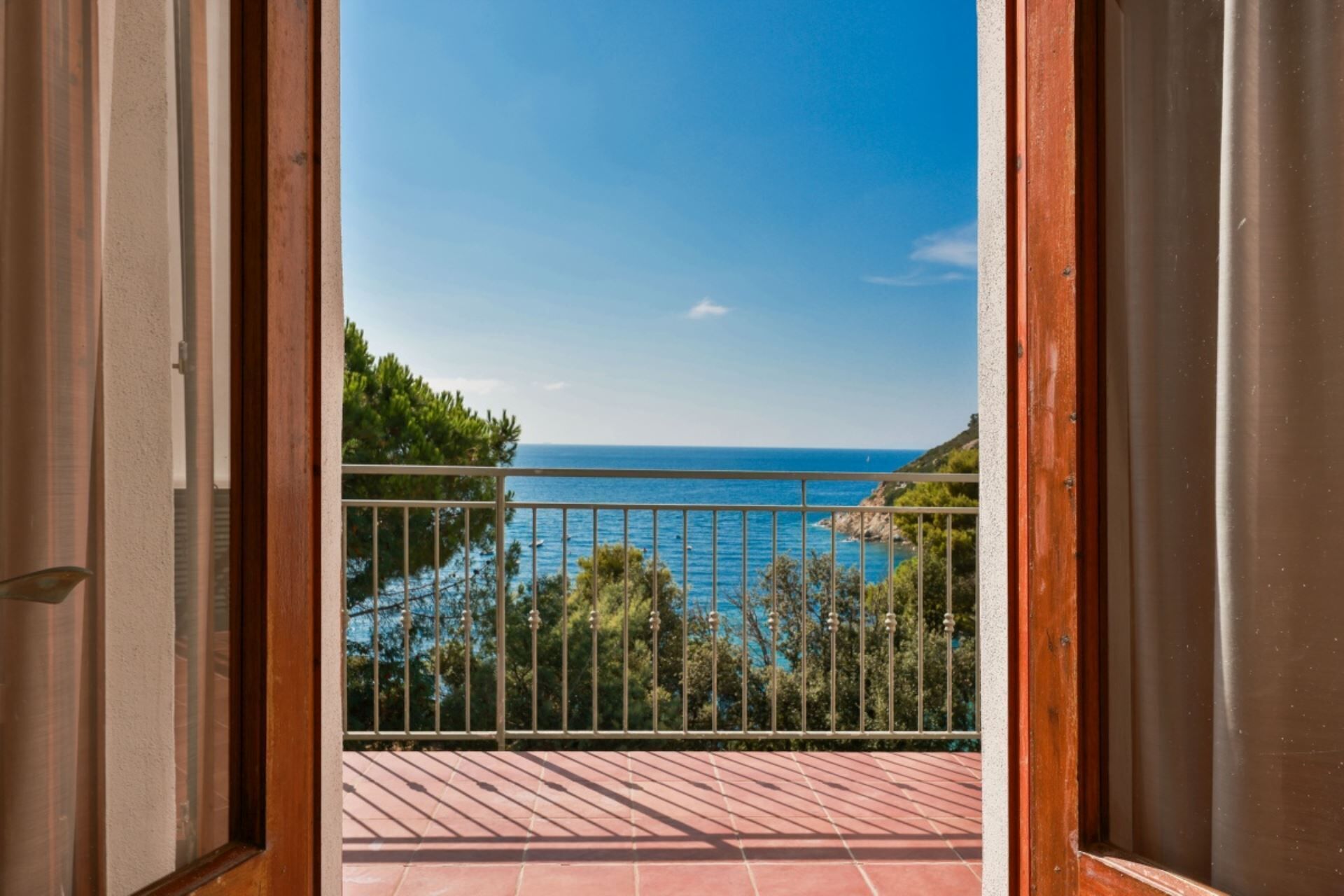 Un balcone con ringhiera in metallo, pavimento piastrellato e vista sul mare e sul verde.
