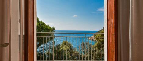 A balcony with a metal railing, a tiled floor, and a view of the sea and greenery.