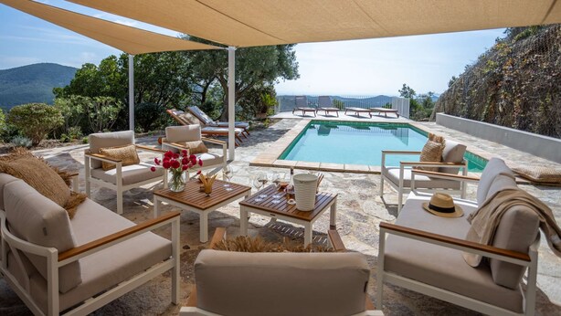 Ein Poolbereich mit Liegestühlen, einem Tisch mit Getränken und Blick auf das Meer und die Berge.