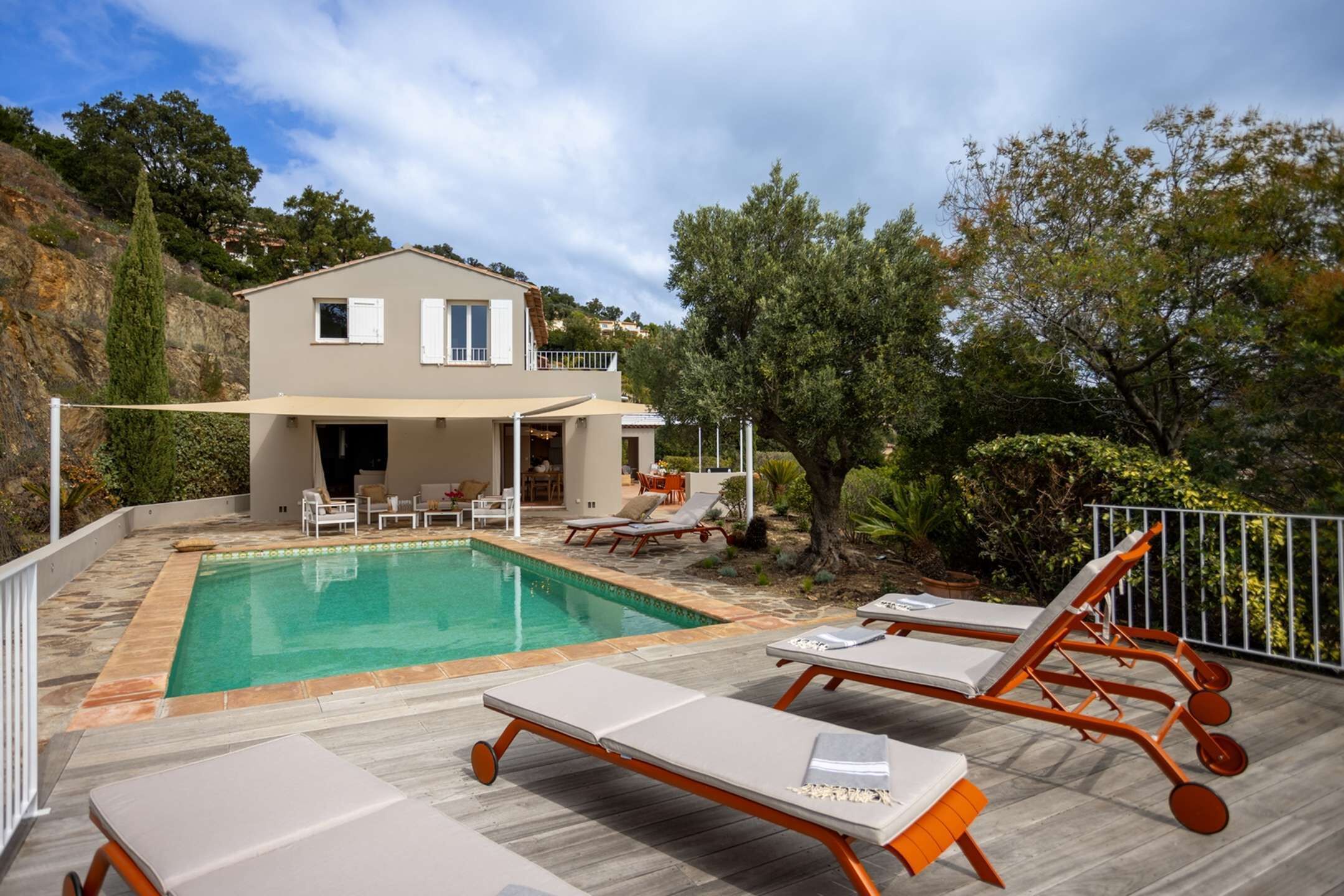 Zona de piscina con sillones de descanso, una casa al fondo y un paisaje montañoso.