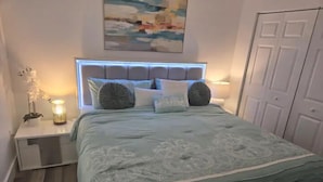 Een slaapkamer met een bed, nachtkastjes, een lamp en een schilderij aan de muur.