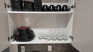 Een keuken met een witte plank waarop zwarte mokken en glazen staan, een stapel rode borden, en een tablet met een afbeelding van een zonsondergang.