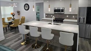 Een moderne keuken met een centraal eiland, barstoelen, roestvrijstalen apparatuur en hanglampen.